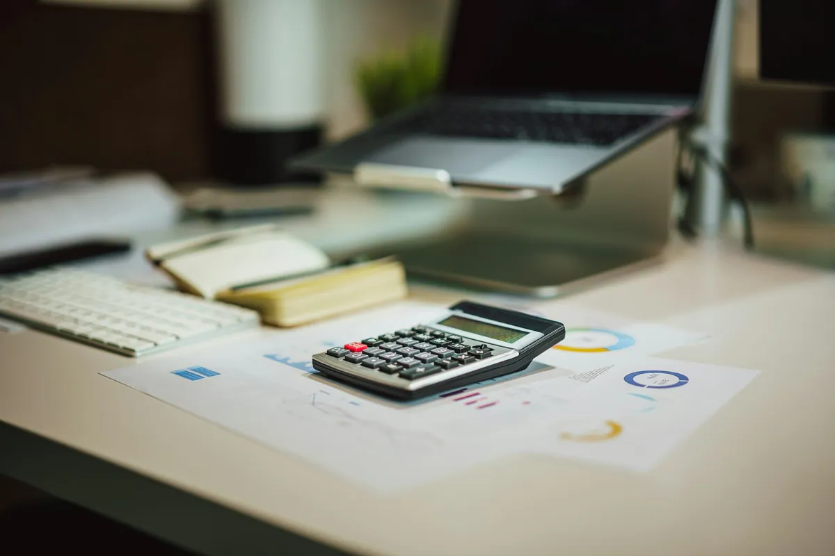 Calculator and printed charts beside a laptop