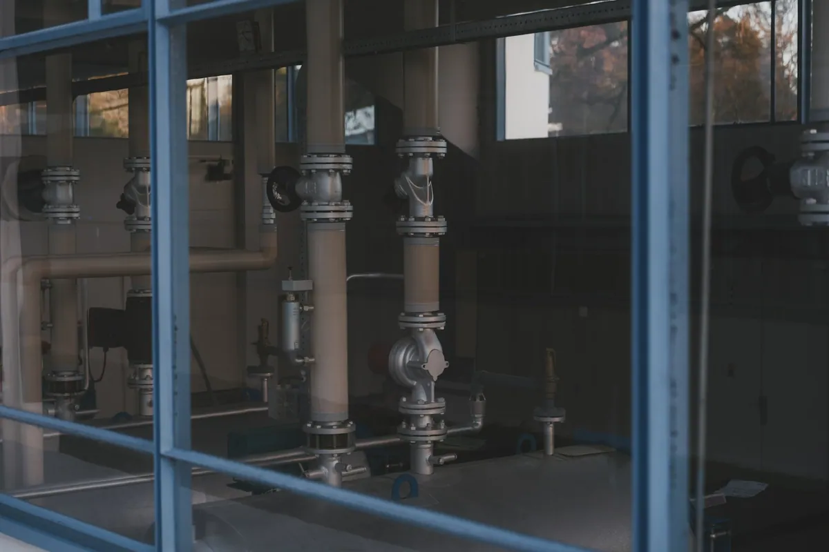 Industrial pipes, valves and gauges visible through the windows of a plant room